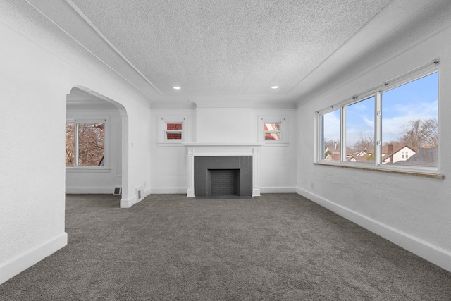 unfurnished living room featuring a wealth of natural light, a fireplace, a textured ceiling, and dark colored carpet