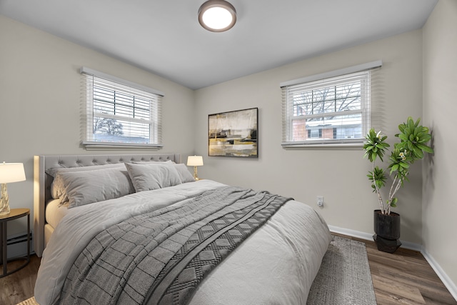 bedroom with wood-type flooring, multiple windows, and a baseboard heating unit