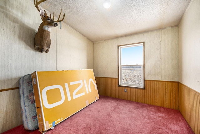 unfurnished room with vaulted ceiling, carpet floors, a textured ceiling, and wood walls