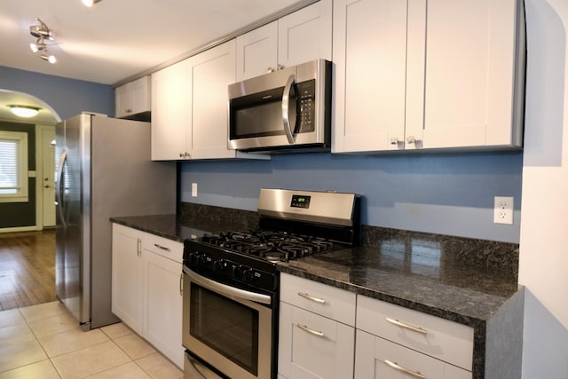 kitchen with dark stone countertops, appliances with stainless steel finishes, light tile patterned floors, and white cabinets