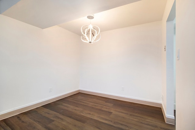 spare room with dark wood-type flooring and a chandelier