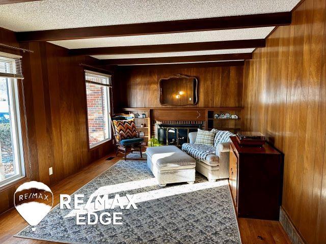 living area with beam ceiling, wood-type flooring, a wealth of natural light, and wooden walls