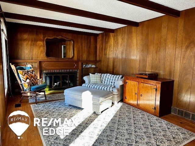 sitting room with beam ceiling, wooden walls, a fireplace, wood-type flooring, and a textured ceiling