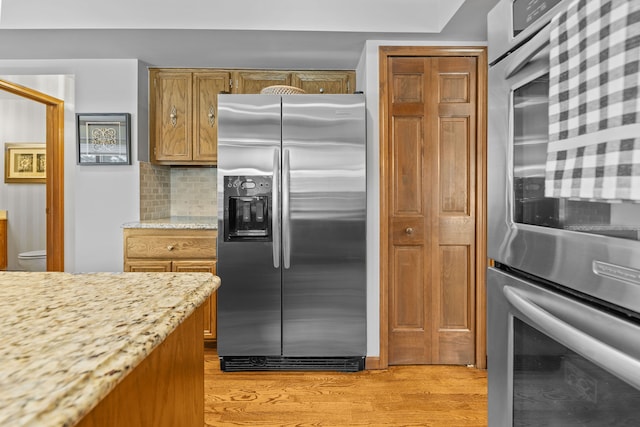 kitchen featuring appliances with stainless steel finishes, decorative backsplash, light stone counters, and light hardwood / wood-style flooring