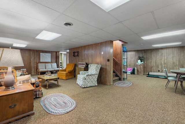 living room with carpet, a paneled ceiling, and wood walls