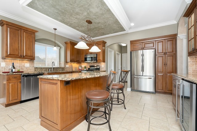 kitchen featuring a center island, hanging light fixtures, appliances with stainless steel finishes, beverage cooler, and light stone countertops