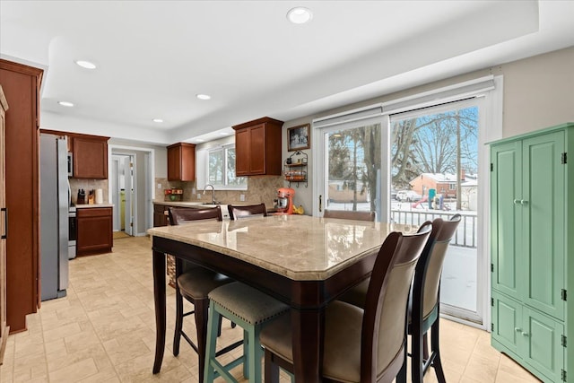 kitchen featuring a kitchen island, stainless steel refrigerator, backsplash, a kitchen bar, and light stone countertops