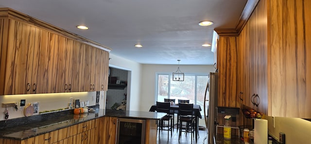 kitchen with stainless steel refrigerator, hanging light fixtures, wine cooler, kitchen peninsula, and dark stone counters