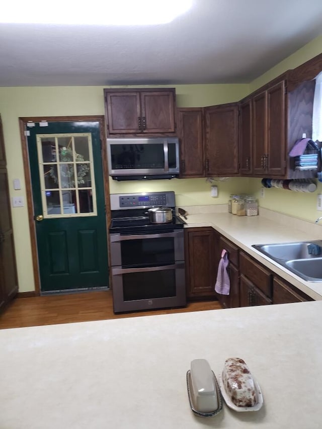 kitchen with light hardwood / wood-style flooring, stainless steel appliances, dark brown cabinets, and sink