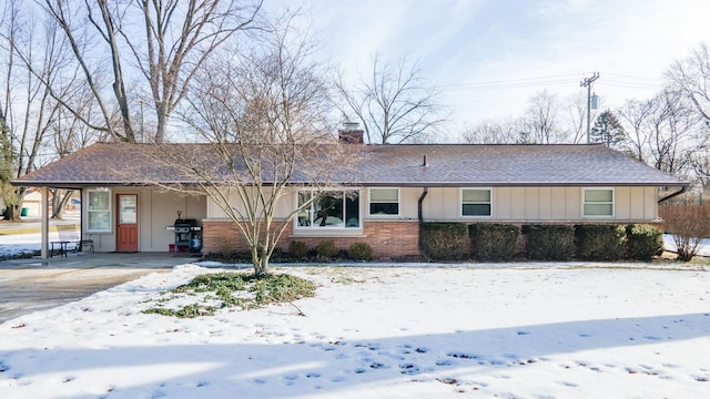 ranch-style home featuring roof with shingles, brick siding, a chimney, and board and batten siding