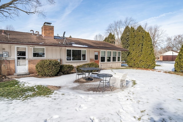 snow covered house featuring board and batten siding, brick siding, and a chimney