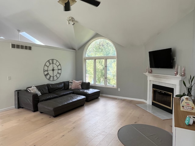 living room with a tile fireplace, lofted ceiling, ceiling fan, and light wood-type flooring