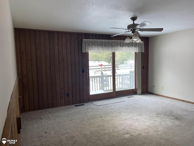 unfurnished room with ceiling fan, carpet floors, a textured ceiling, and wood walls