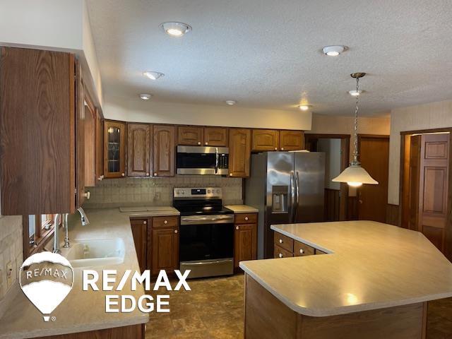 kitchen featuring sink, a kitchen island, pendant lighting, stainless steel appliances, and decorative backsplash