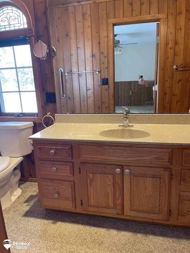 bathroom featuring wooden walls, a healthy amount of sunlight, toilet, and vanity