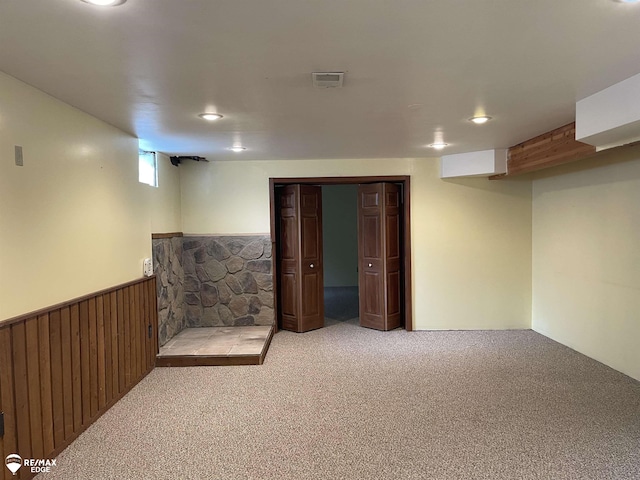 basement featuring light colored carpet and wooden walls