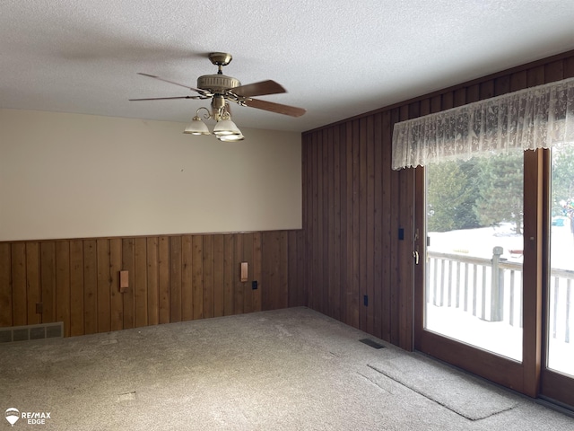 carpeted spare room featuring ceiling fan, a textured ceiling, and wooden walls