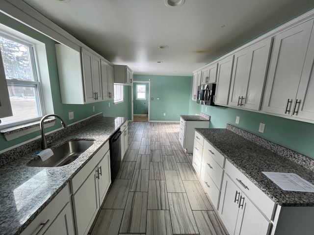 kitchen with stainless steel microwave, wood finish floors, a sink, and dark stone countertops
