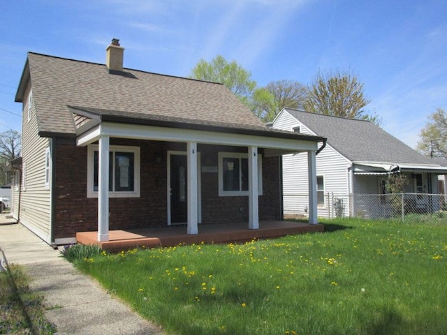 rear view of property featuring fence, covered porch, a chimney, a shingled roof, and a lawn