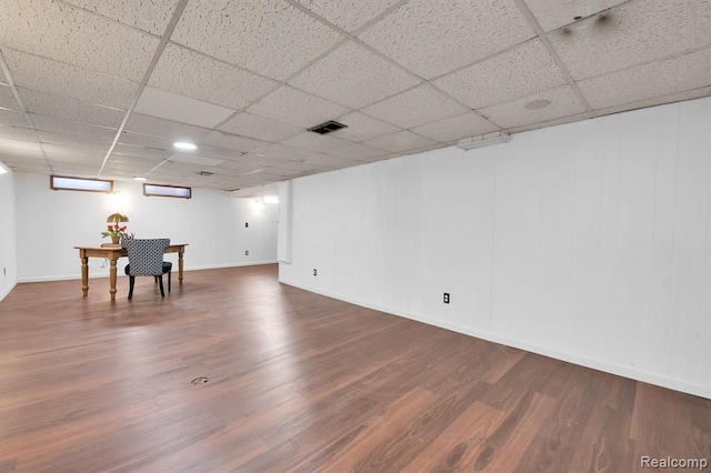 basement featuring wood-type flooring, an AC wall unit, and a paneled ceiling