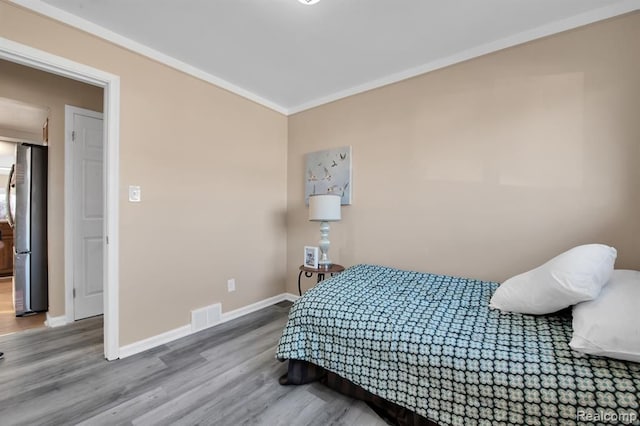 bedroom featuring wood-type flooring, ornamental molding, and stainless steel refrigerator