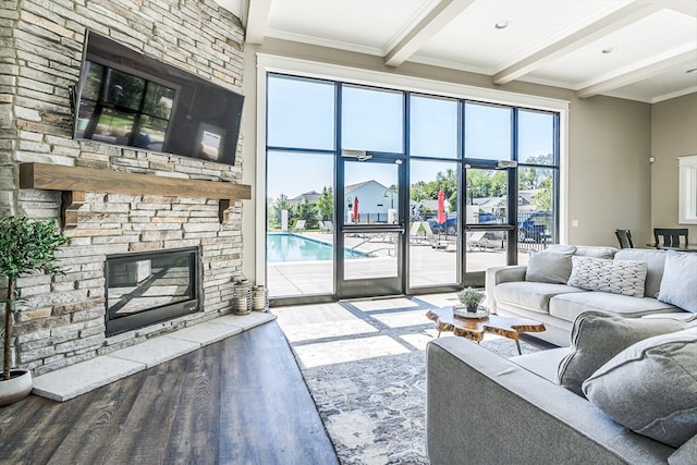 living room with a stone fireplace, wood-type flooring, ornamental molding, and beamed ceiling