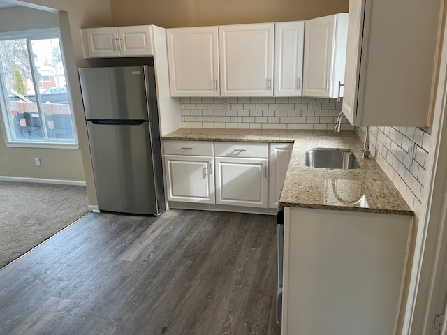 kitchen with stainless steel refrigerator, white cabinetry, light stone countertops, and sink