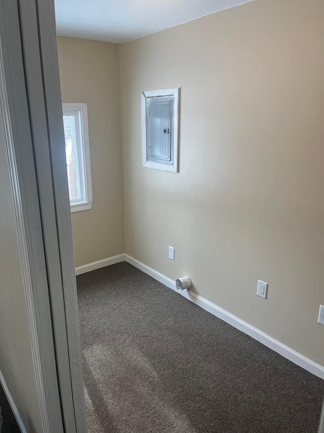 empty room featuring dark carpet, baseboards, and electric panel