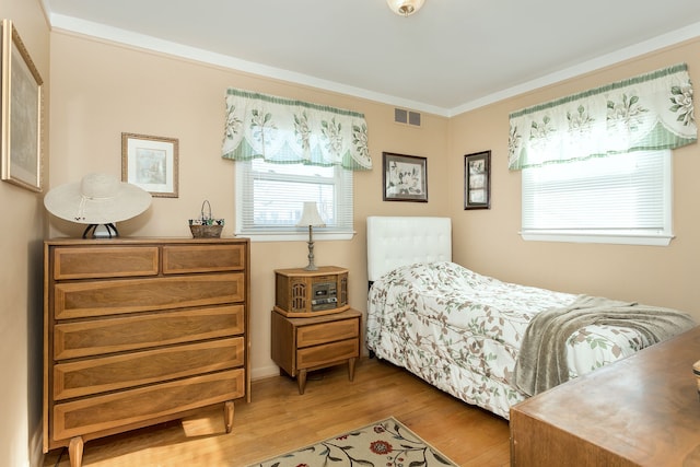 bedroom with wood finished floors, visible vents, and crown molding