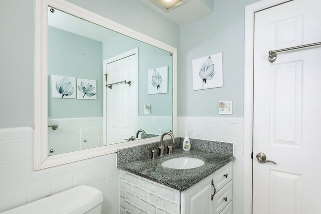 bathroom with tile walls, a wainscoted wall, vanity, and toilet