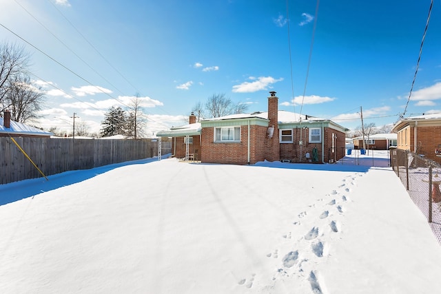 snow covered property with a chimney, fence, and brick siding