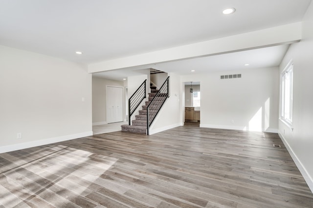 empty room featuring a healthy amount of sunlight, stairway, and wood finished floors