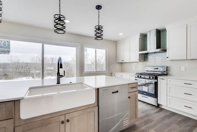 kitchen with stainless steel appliances, light countertops, white cabinetry, a sink, and wall chimney range hood