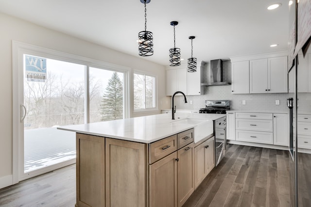 kitchen with a kitchen island with sink, a sink, white cabinets, light countertops, and wall chimney exhaust hood