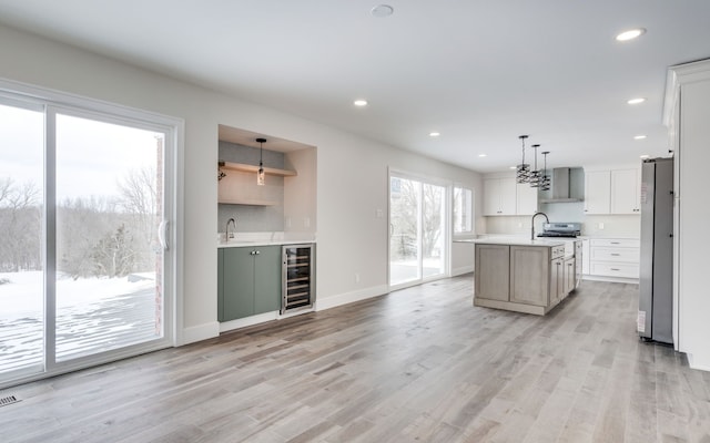 kitchen featuring beverage cooler, light countertops, an island with sink, and pendant lighting