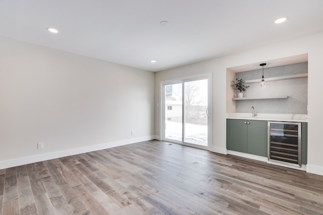 bar with wine cooler, indoor wet bar, hanging light fixtures, a sink, and wood finished floors