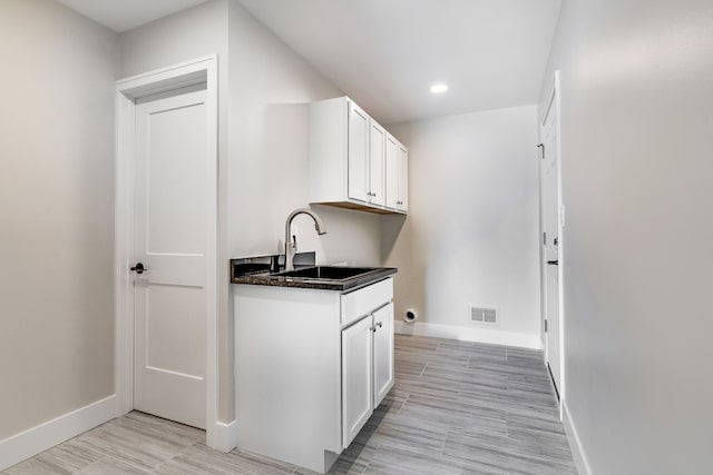 kitchen with baseboards, visible vents, white cabinets, dark countertops, and a sink