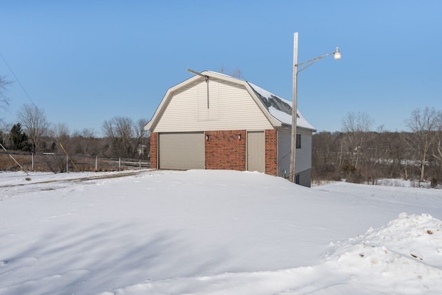 view of snow covered exterior featuring brick siding and a gambrel roof