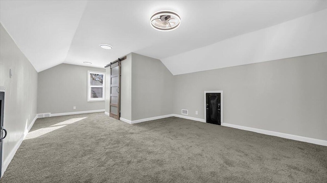 additional living space with vaulted ceiling, a barn door, and carpet