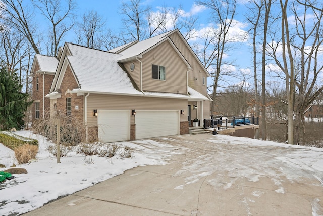 view of snow covered exterior with a garage, central AC, brick siding, and driveway