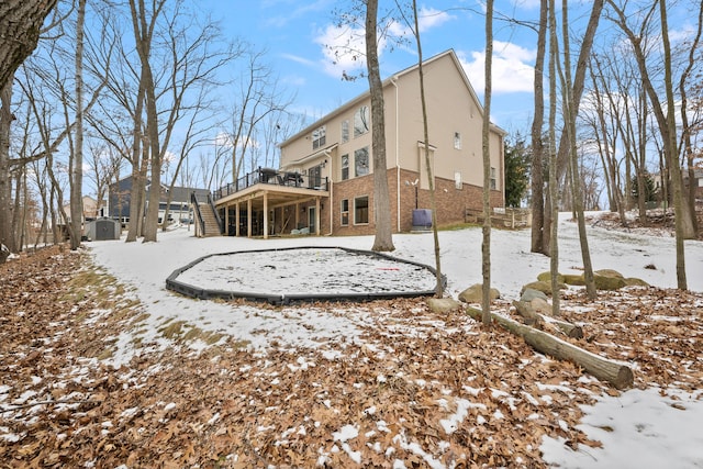 snow covered property with brick siding, a deck, and stairs