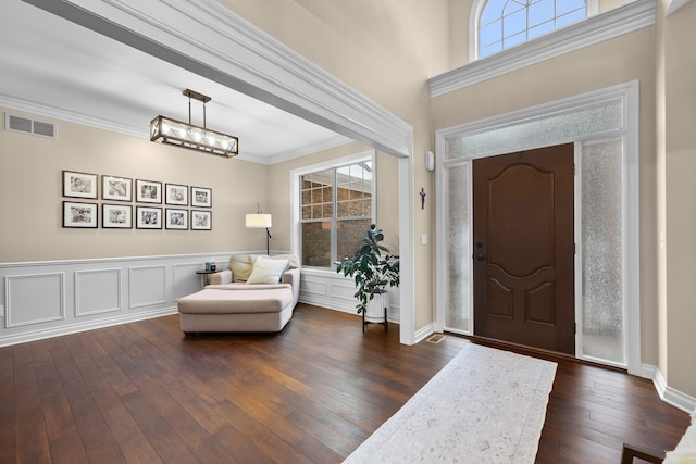 entrance foyer featuring dark wood-style floors, visible vents, a decorative wall, and crown molding