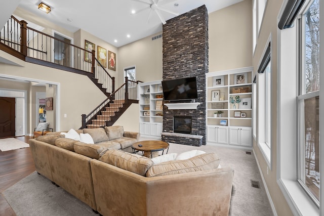 living room with stairway, a stone fireplace, visible vents, and a towering ceiling