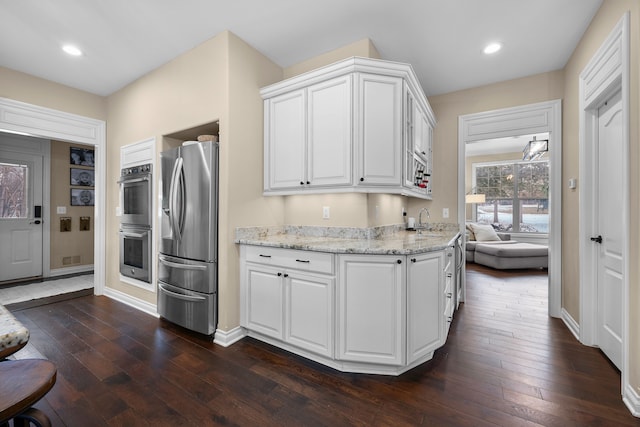 kitchen featuring white cabinets, light stone counters, stainless steel appliances, and dark wood-type flooring