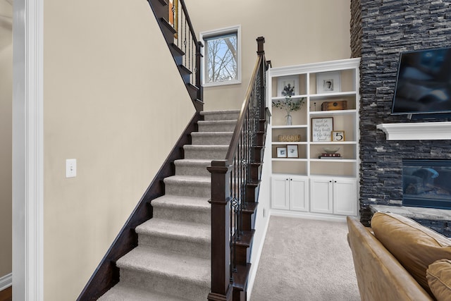 staircase with carpet flooring and a stone fireplace