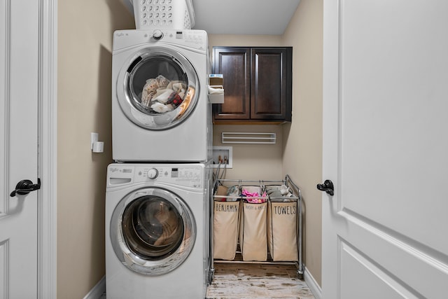 washroom with cabinet space, baseboards, and stacked washer / dryer