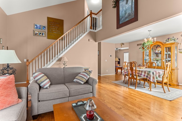 living room featuring hardwood / wood-style flooring, a towering ceiling, and ceiling fan with notable chandelier