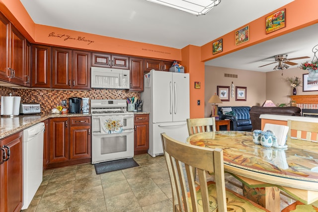 kitchen with light stone counters, ceiling fan, dark tile patterned floors, white appliances, and decorative backsplash