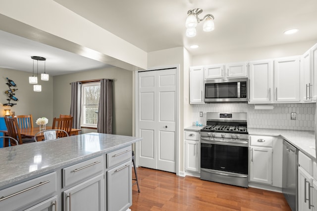 kitchen featuring hanging light fixtures, light wood-type flooring, appliances with stainless steel finishes, decorative backsplash, and white cabinets