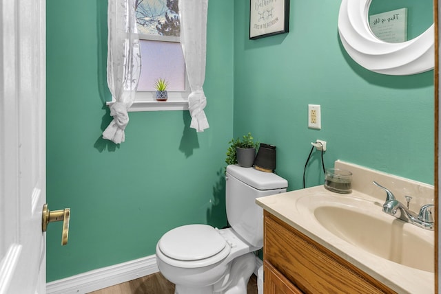 half bath featuring baseboards, toilet, wood finished floors, and vanity